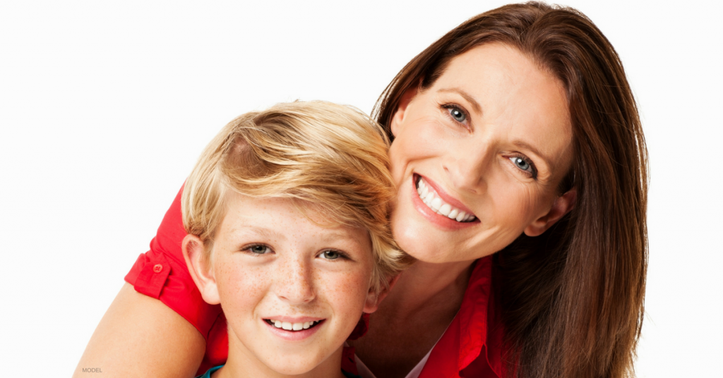 Face of dark-haired middle aged woman smiling with arm around smiling blonde boy